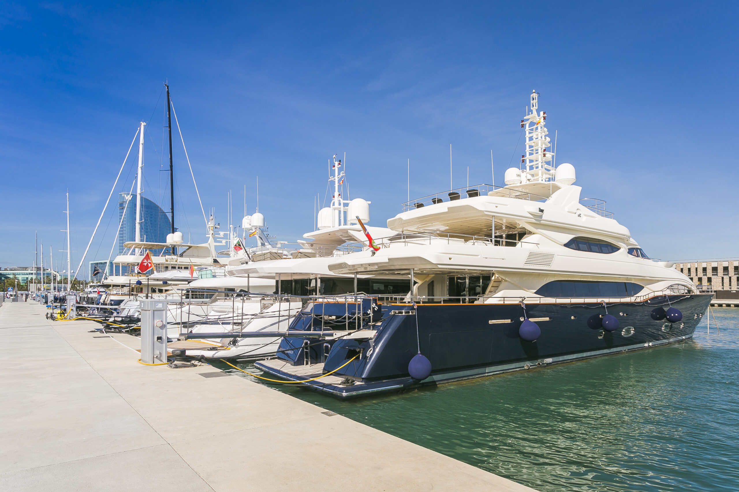 Luxury yachts docked at a marina on a sunny day with clear blue skies.