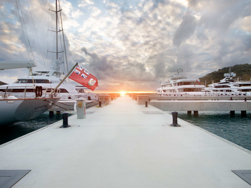 A marina dock at sunset with luxury yachts moored on both sides and the CH flag visible on one yacht.