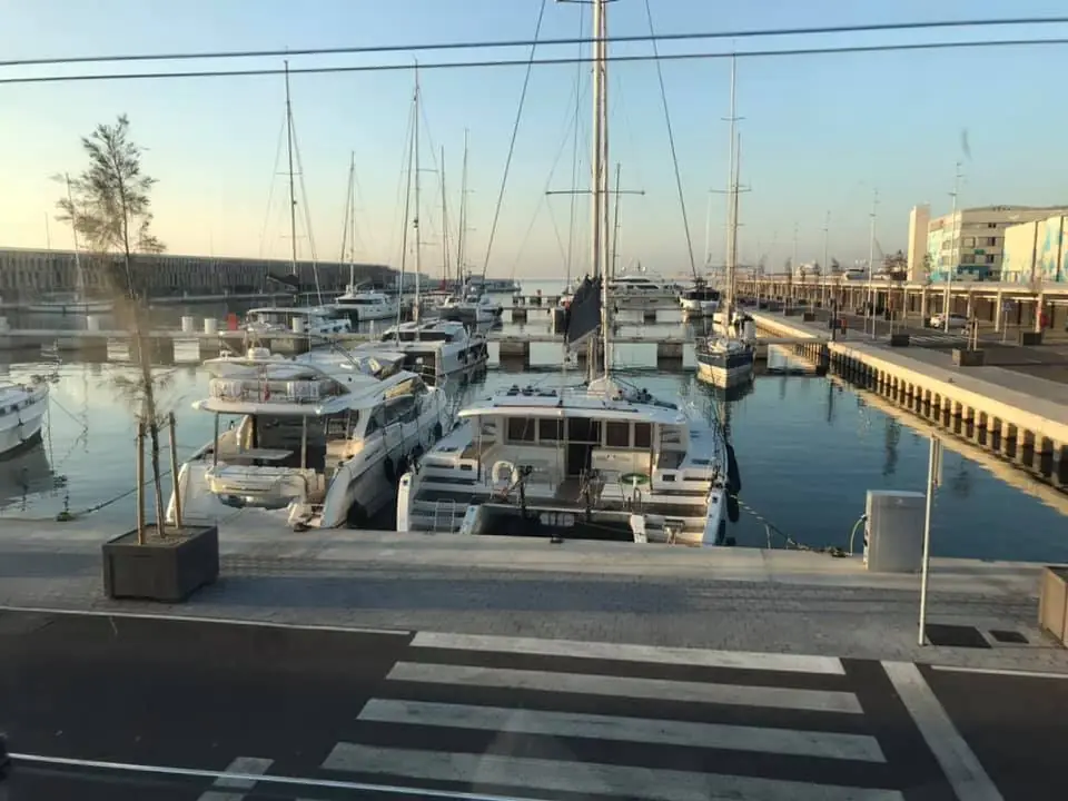 Several yachts are docked in a marina in front of the Capitainerie building at sunset.
