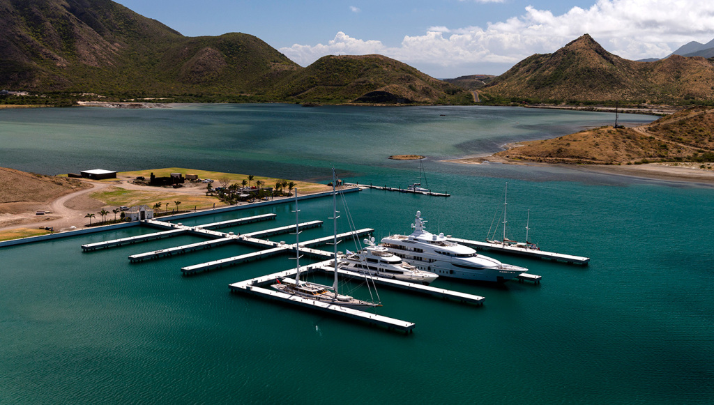 Luxury yachts docked at Christophe Harbour marina with scenic mountains and turquoise waters in the background.
