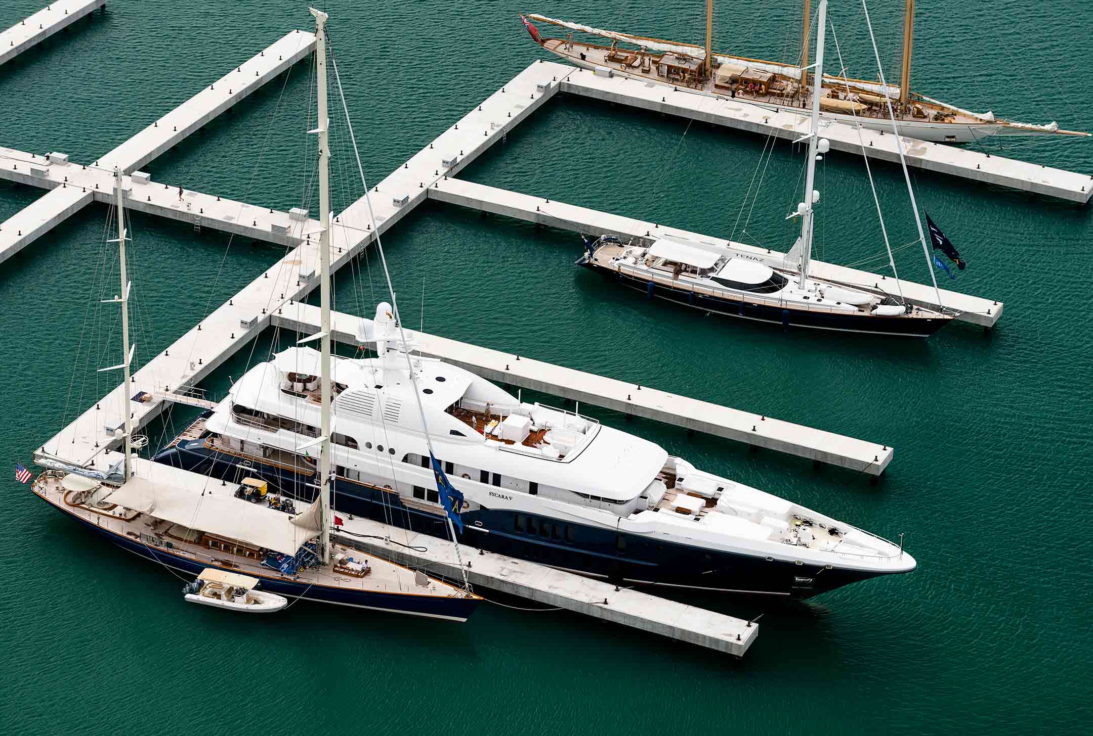 Several luxury yachts, including the Christophe Kitts 18A, docked at a modern marina in turquoise waters.