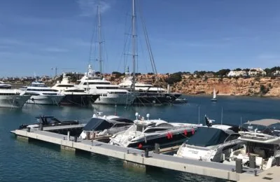 Luxusyachten, die in einem Yachthafen vor Anker liegen, mit Klippen und Häusern im Hintergrund unter einem klaren blauen Himmel.