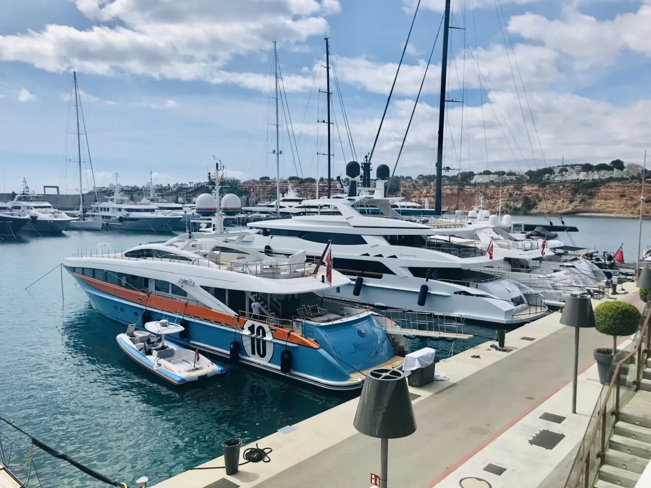 Luxusjachten in einem Yachthafen mit klarem, blauem Wasser und einer felsigen Küstenlinie im Hintergrund.