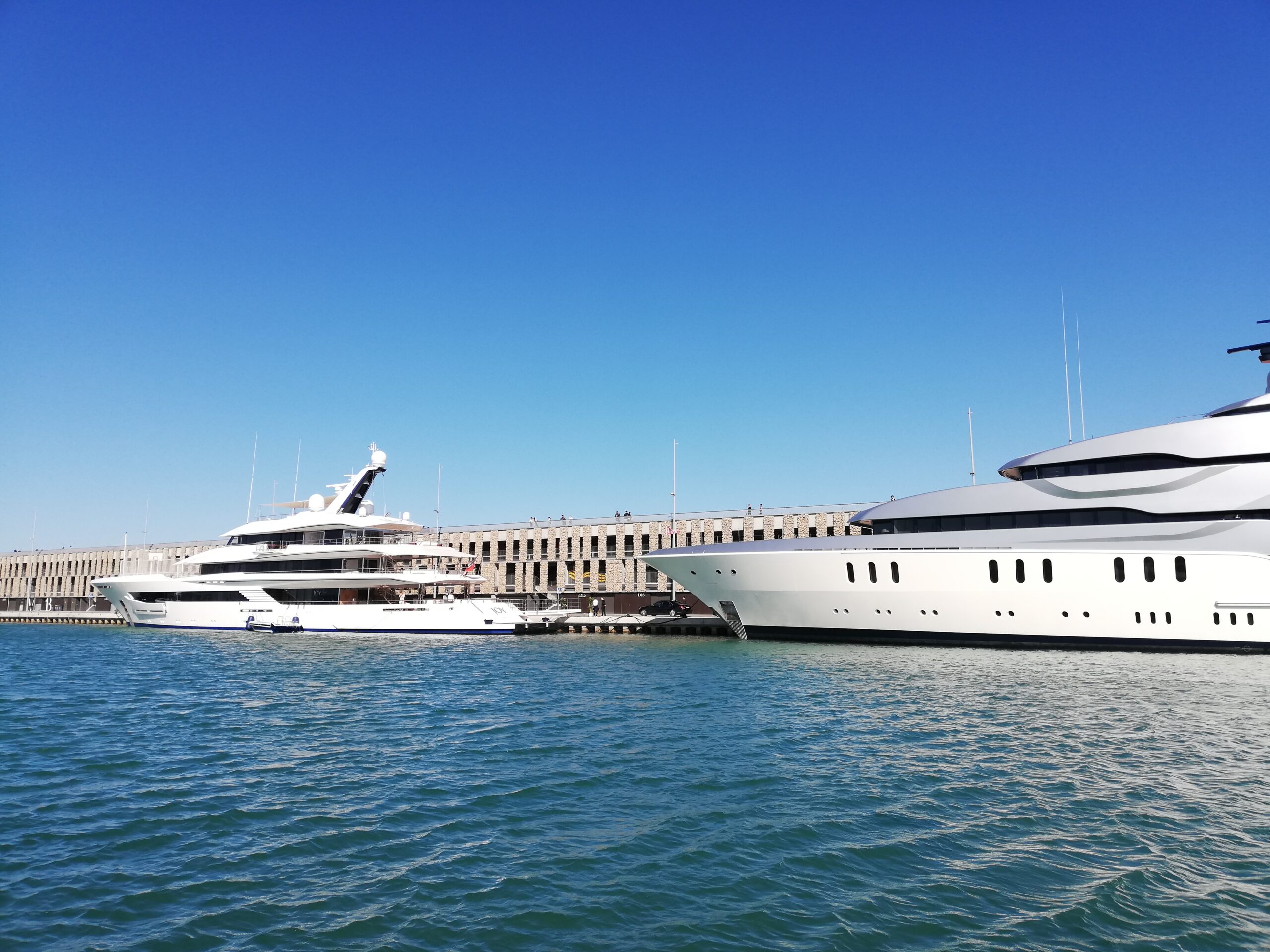 Two luxurious yachts docked at a pier with a clear blue sky in the background.