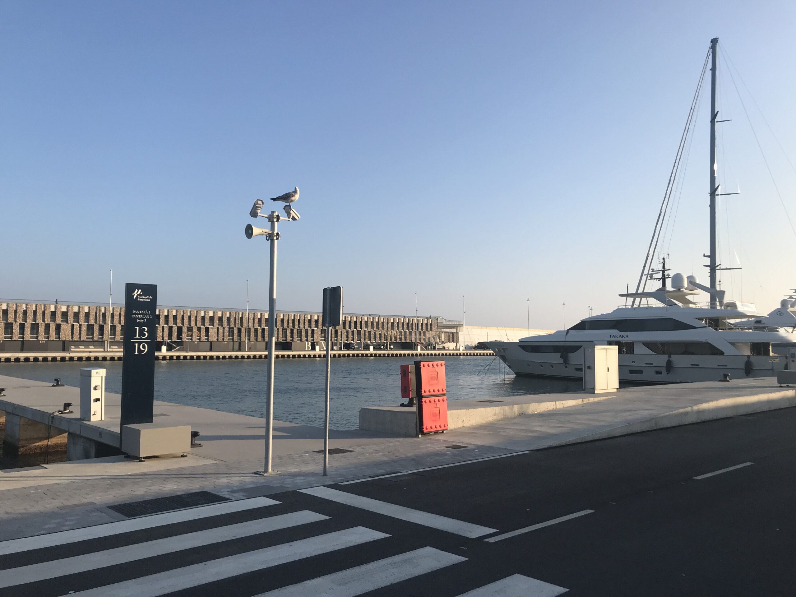 Luxury yacht named "TAKARA" docked at a modern marina near pontoon 13–19 under a clear blue sky.