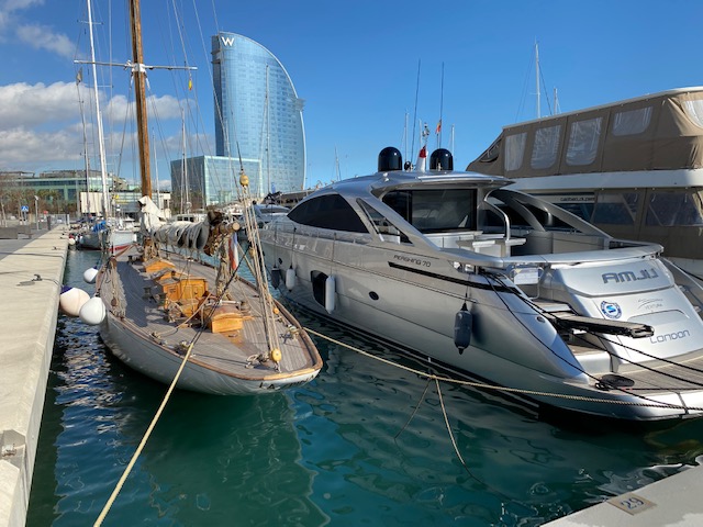 A classic wooden sailboat and a modern MV20202 motor yacht docked side by side in a sunny marina.