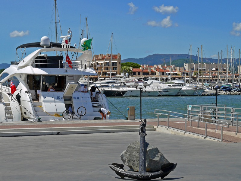 Luxury yachts moored at Marines de Cogolin marina in France with a large anchor monument in the foreground.