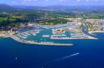 Luftaufnahme des Yachthafens von Marines de Cogolin in Frankreich, der mit vor Anker liegenden Yachten gefüllt und von Gebäuden an der Küste umgeben ist.
