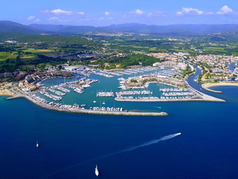Aerial view of the marina at Marines de Cogolin in France, filled with moored yachts and surrounded by coastal buildings.