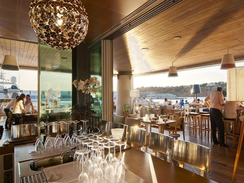 Modern waterfront restaurant with a view of Port Adriano marina in Mallorca at sunset.