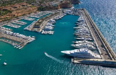 Luftaufnahme des luxuriösen Yachthafens Port Adriano, der mit Yachten gefüllt und von klarem, blauem Wasser umgeben ist.