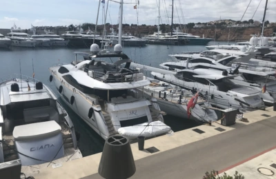 Luxusyachten, die in einem Yachthafen angedockt haben, darunter die Boote mit den Namen "DIANA", "SKL" und "Naos", unter einem teilweise bewölkten Himmel.