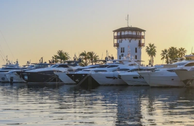 Luxusyachten, die bei Sonnenuntergang in einem Yachthafen mit einem weißen Turm und Palmen vor Anker lagen.