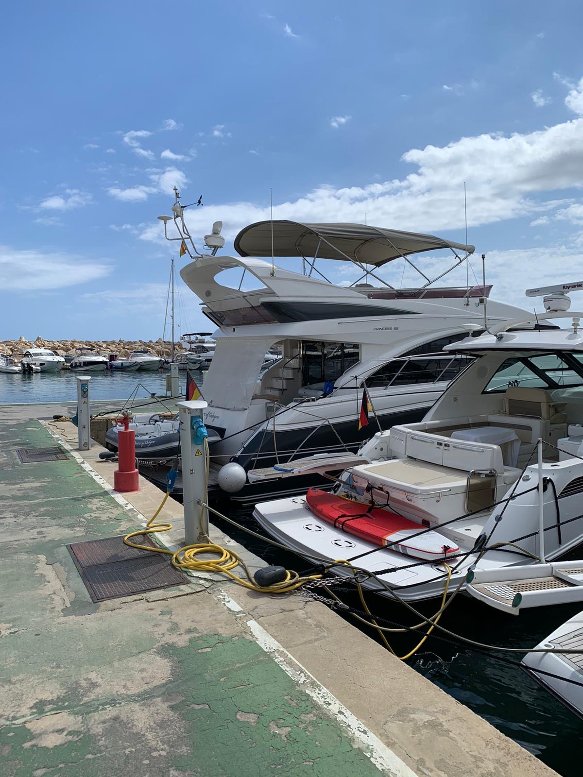 Luxury yachts are docked at a marina on a sunny day with clear skies.