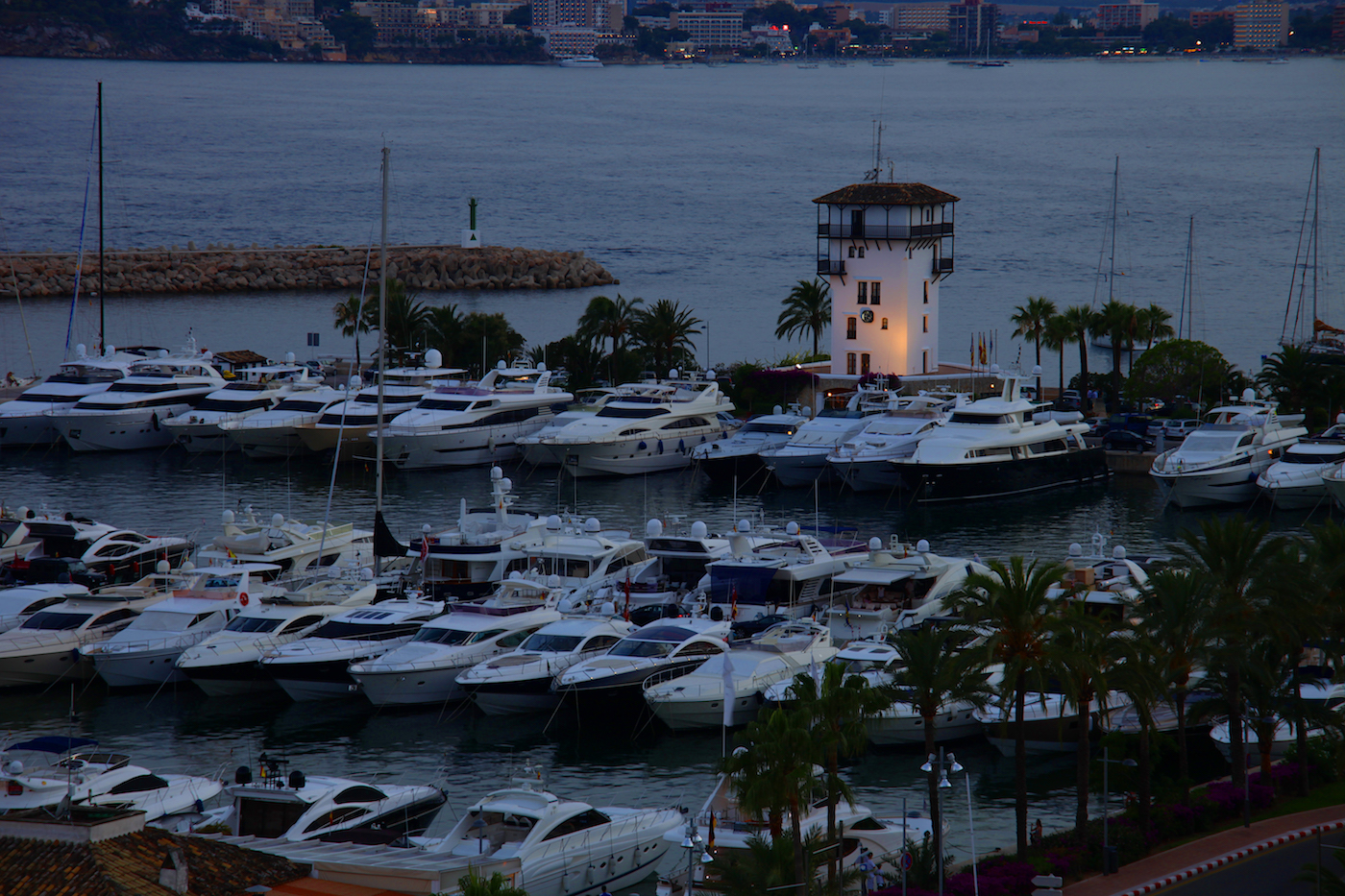 A luxury marina filled with yachts at dusk in Portals Nous, with the iconic Lengers tower illuminated near the waterfront.
