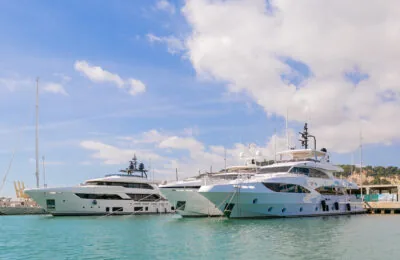 Luxury yachts docked at Marina Vela in Barcelona under a blue sky with fluffy clouds.