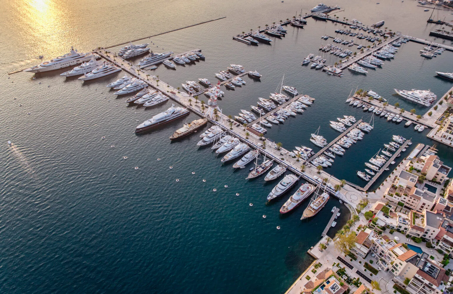 Aerial view of Porto Montenegro marina with numerous luxury yachts docked along piers at sunset.