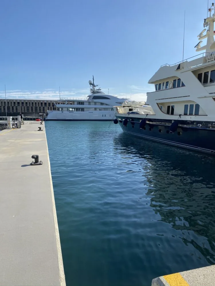 Two luxury yachts docked in a calm marina on a sunny day.