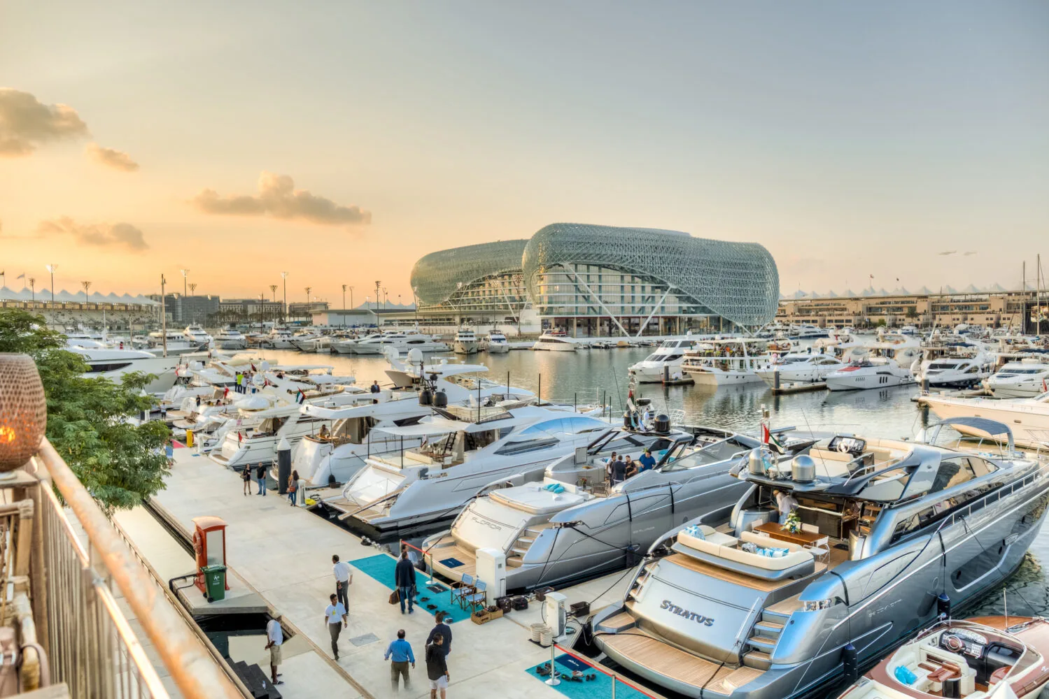 Luxury yachts docked at Yas Marina during a golden sunset with the iconic Yas Hotel in the background.