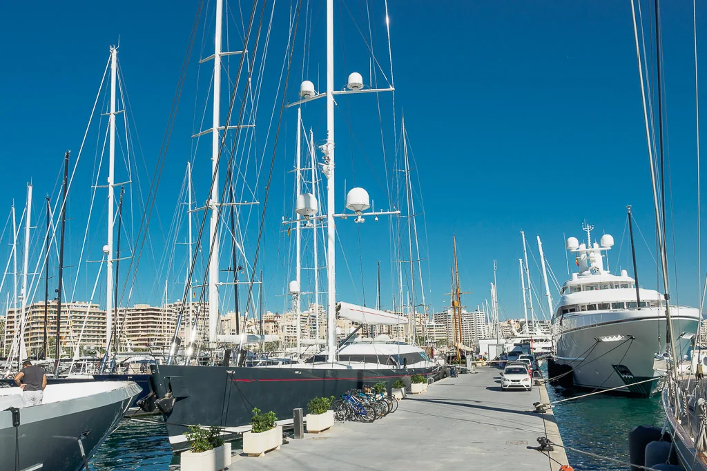 Luxury yachts and sailboats docked at a marina under a clear blue sky.