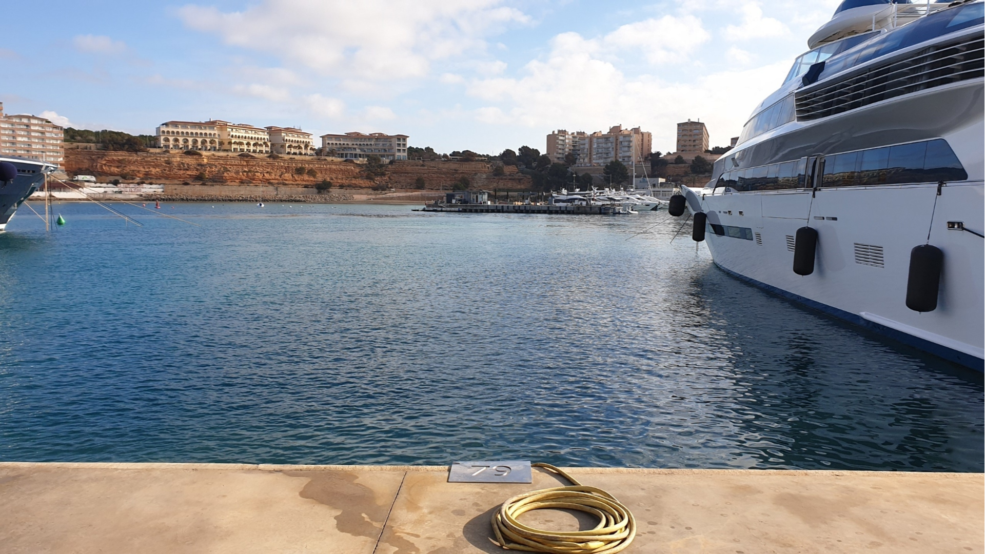 View of berth 79 at Port Adriano with a coiled yellow hose in the foreground and luxury yachts docked in the background.