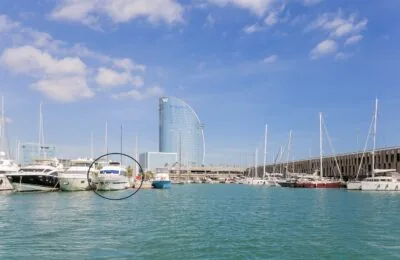 Ein Yachthafen, in dem mehrere Yachten vor Anker liegen, im Hintergrund das Gebäude eines W-Hotels und im Vordergrund ein eingekreistes Boot, das wahrscheinlich auf ein bestimmtes Schiff hinweist.