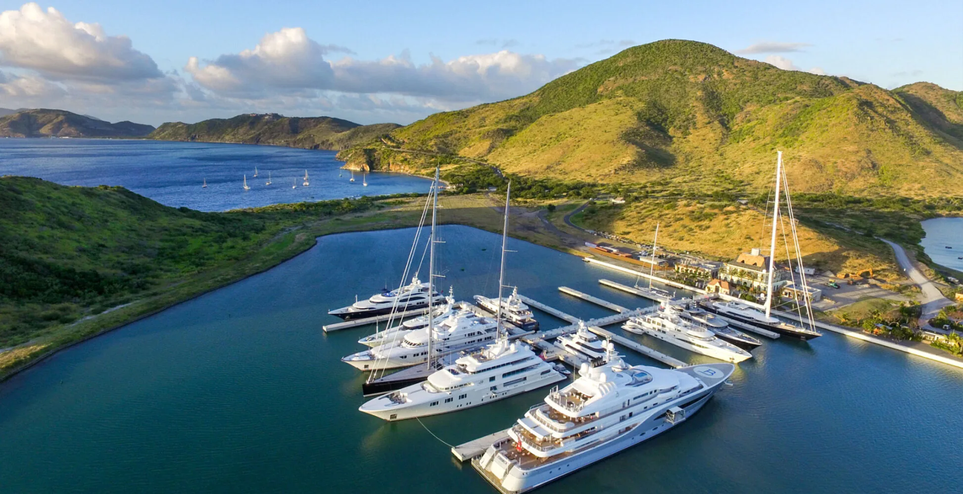 Luxusyachten, die in einem Yachthafen angedockt sind, umgeben von grünen Hügeln und einem ruhigen blauen Meer.
