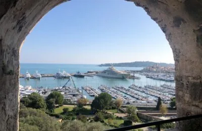 View of Port Vauban through a stone archway, showing numerous yachts and boats docked in the marina.