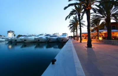 Bei Sonnenuntergang lagen Luxusyachten in einem Yachthafen neben einer von Palmen gesäumten Promenade mit Restaurants vor Anker.