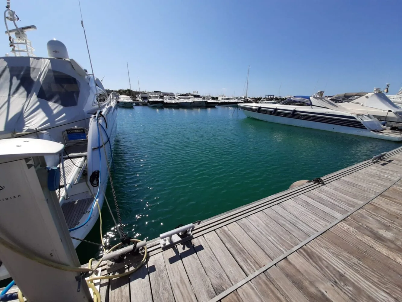 Luxury yachts moored at a sunny marina with clear blue water and a wooden dock.