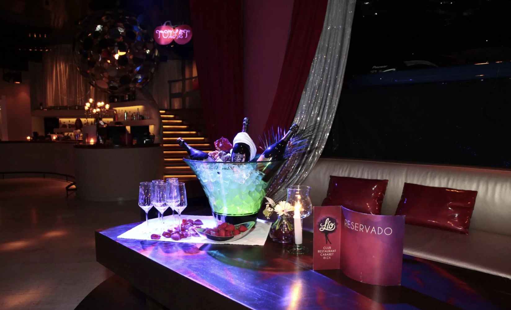 A reserved table at Lío Ibiza with champagne, glasses, and a decorative setting on a stylish couch.