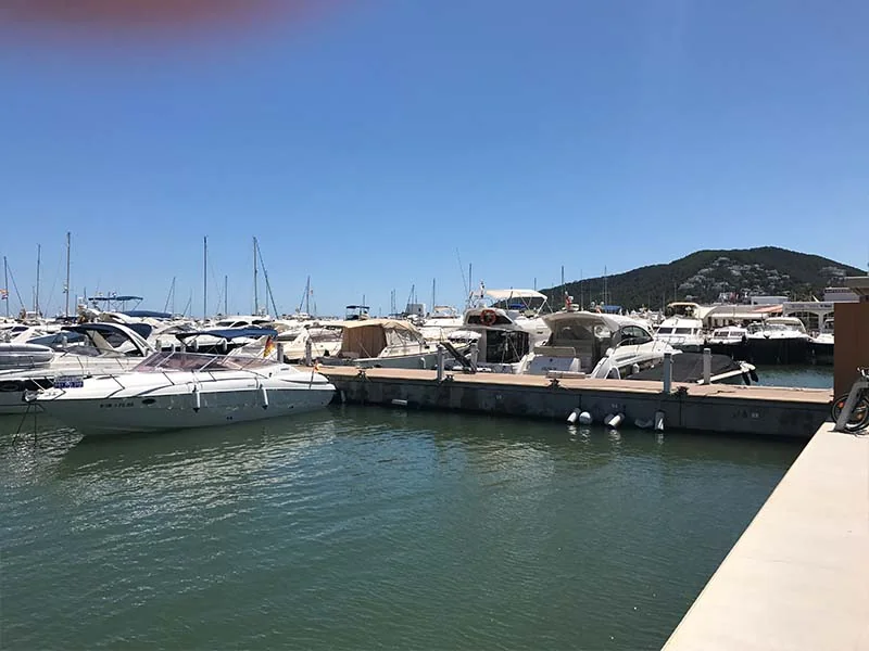 View of a marina in Santa Eulalia with several docked yachts and boats under a clear blue sky.