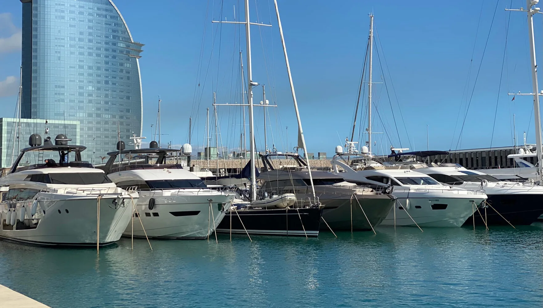 Luxusyachten an einem direkten Liegeplatz in einem modernen Yachthafen mit einem markanten segelförmigen Gebäude im Hintergrund.