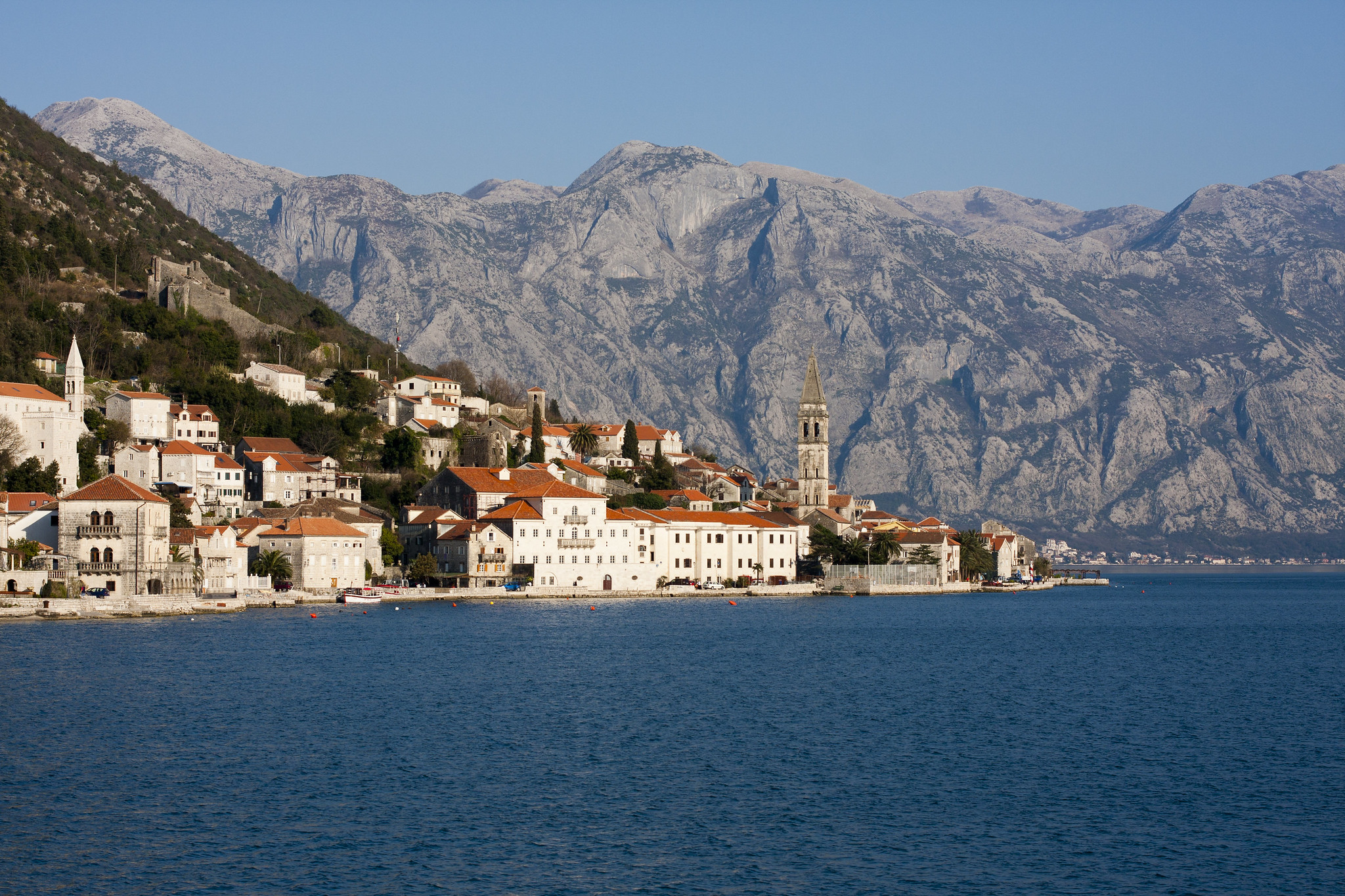 Coastal town of Perast in Montenegro with historic buildings, a church tower, and a mountainous backdrop by the Bay of Kotor.