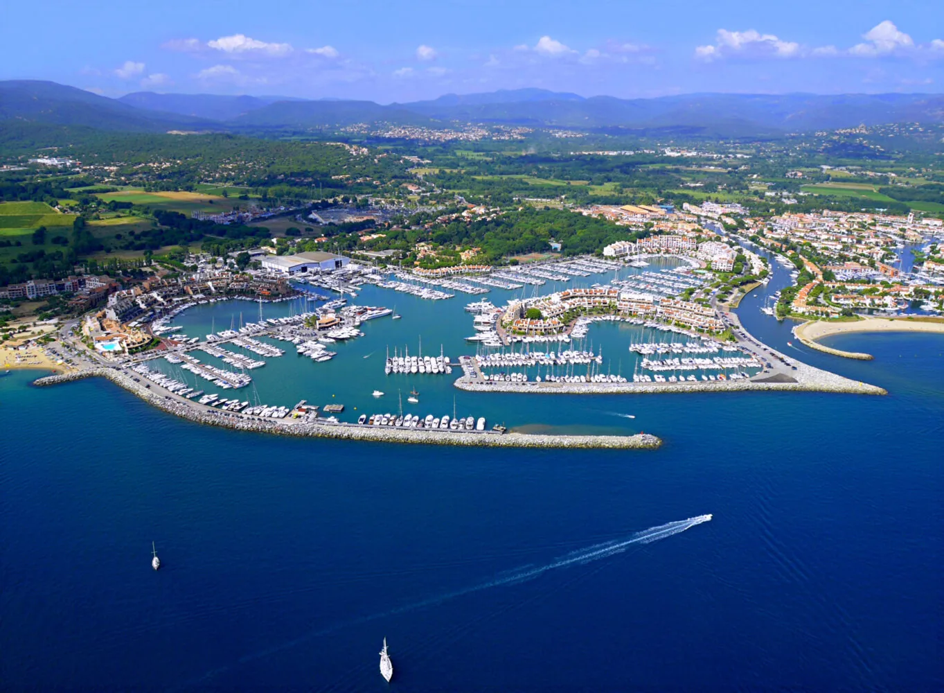 Aerial view of the Cogolin marina on the French Riviera, showing numerous boats, breakwaters, and surrounding buildings.