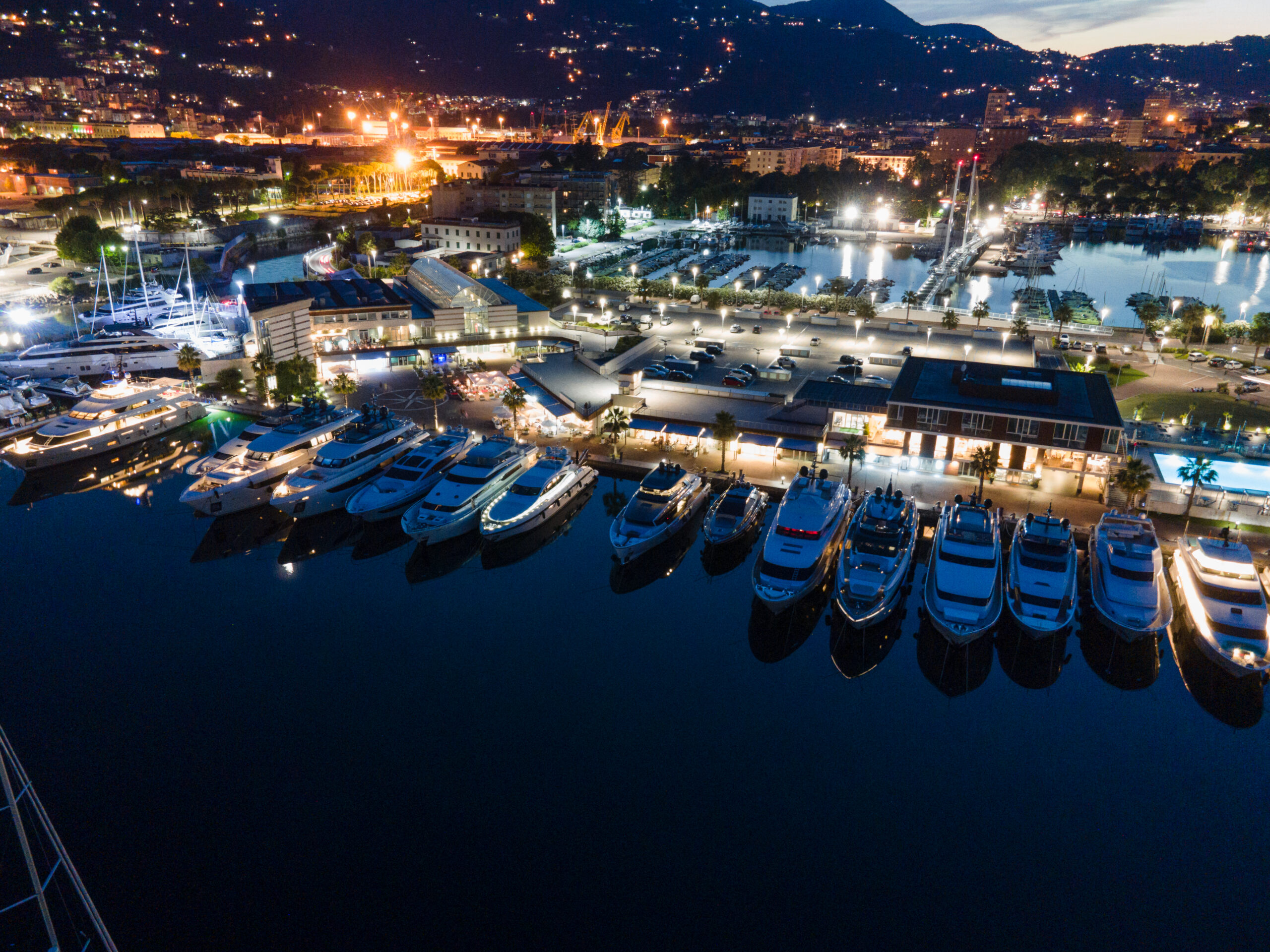 A row of luxury yachts docked at a brightly lit marina during the evening in Dock A.