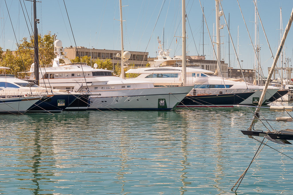 Several luxury yachts are docked in a marina on a sunny day with calm water reflections.