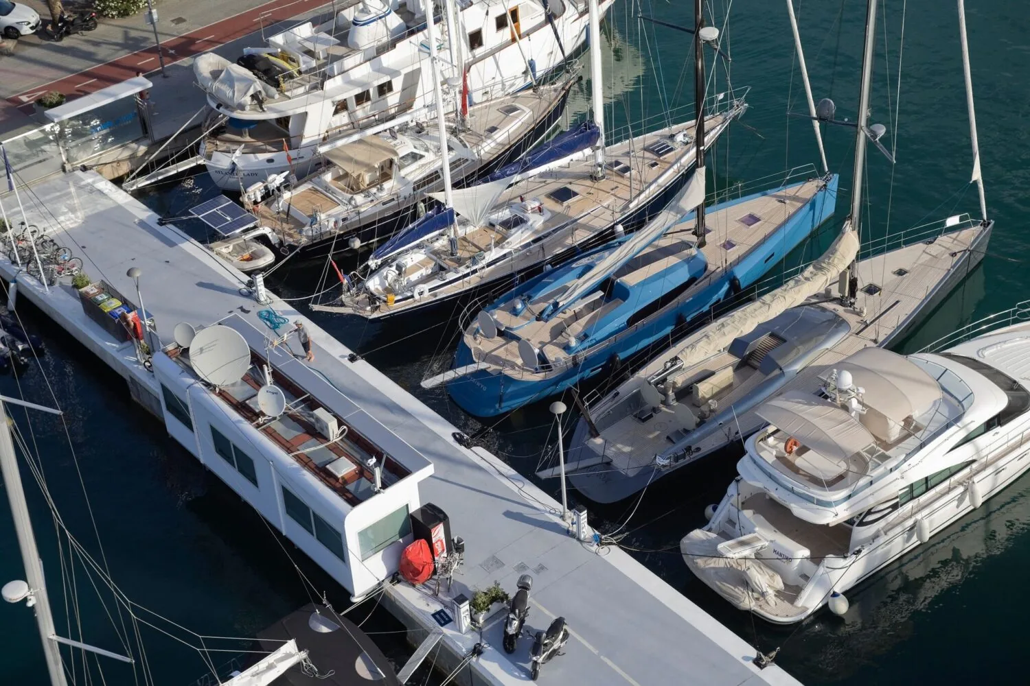 Several luxury yachts are docked side by side at a marina, viewed from above.