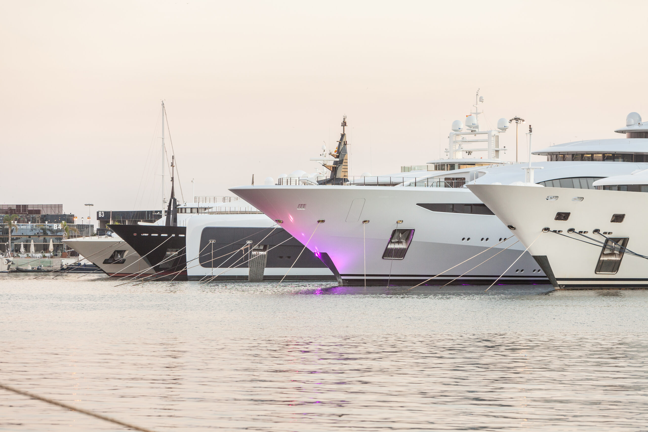 Several luxurious superyachts docked side by side at a marina during sunset.