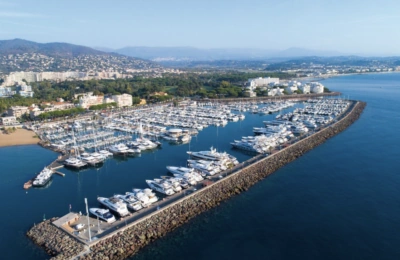 Luftaufnahme des Yachthafens von La Napoule, der mit Yachten und Booten gefüllt ist und von einer Mole sowie einer Küstenstadt umgeben ist.