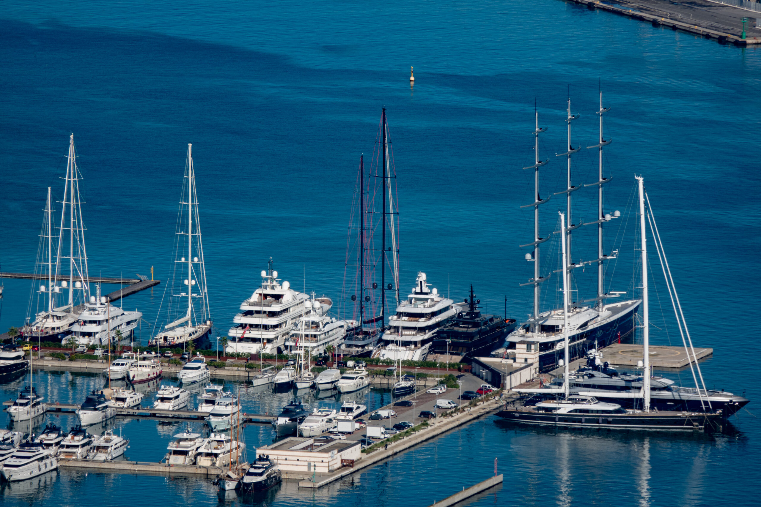 A row of luxury superyachts and sailing yachts docked at the Megayacht Quay in a marina with clear blue water.