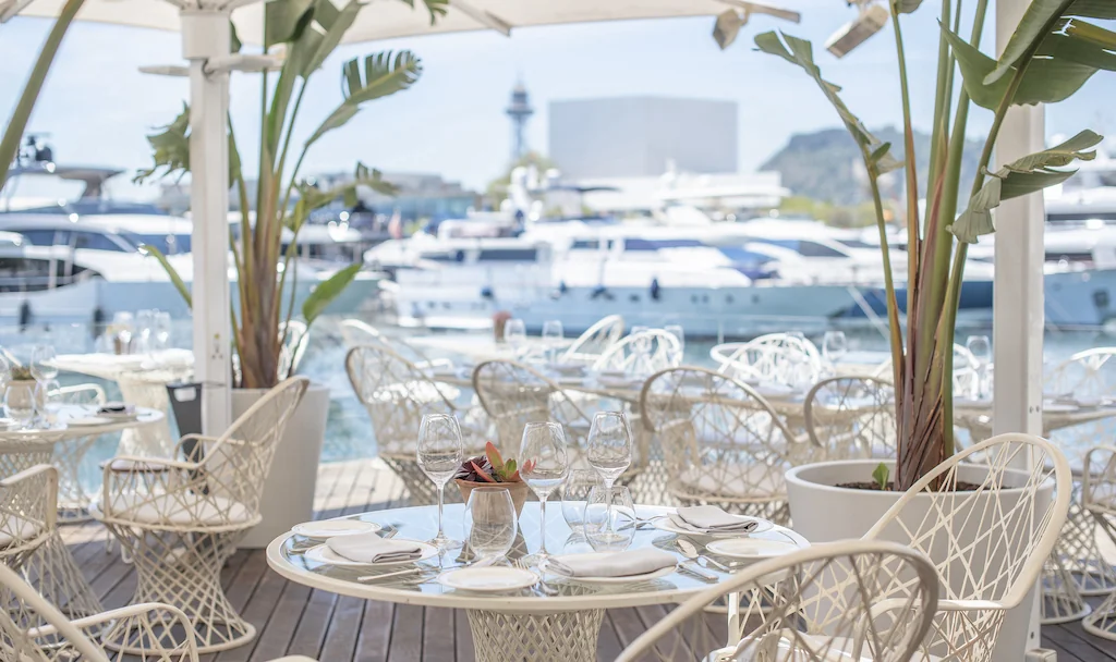 Outdoor dining area at MPVR restaurant with elegant white furniture overlooking a marina filled with yachts.