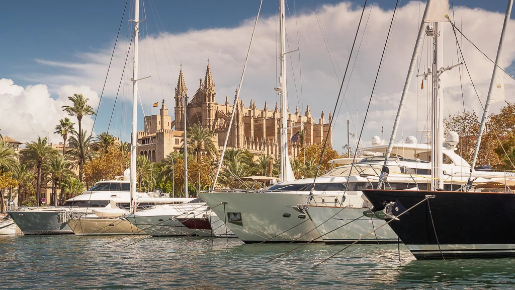 Luxury yachts docked at Marina Moll Vell in Mallorca with the cathedral in the background.