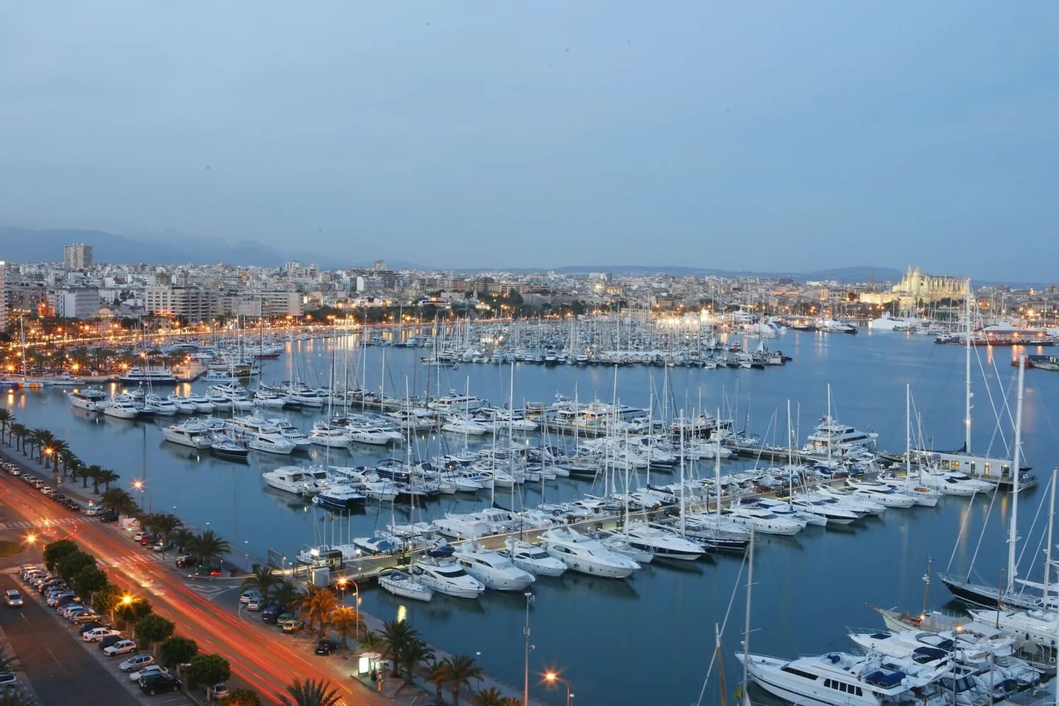 Evening view of the PDM3 marina in Palma de Mallorca with numerous yachts and the illuminated city skyline in the background.