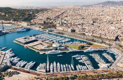 Aerial view of Port Vell in Barcelona, showing a marina filled with yachts and boats against the backdrop of the city skyline.