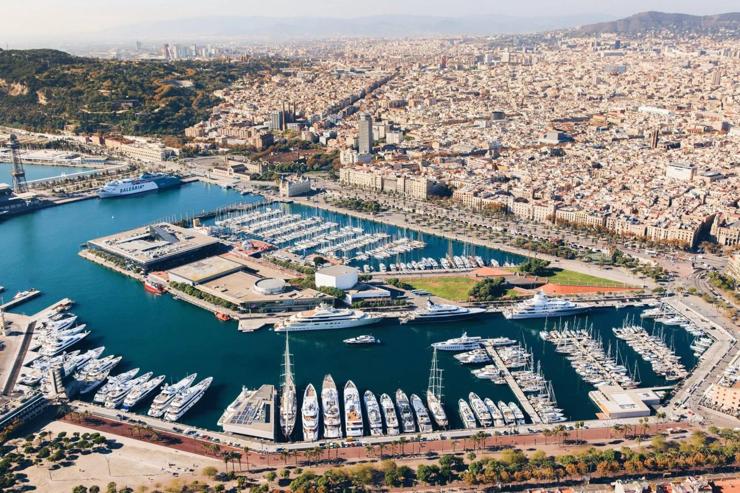 Aerial view of Port Vell in Barcelona, showing a marina filled with yachts and boats against the backdrop of the city skyline.