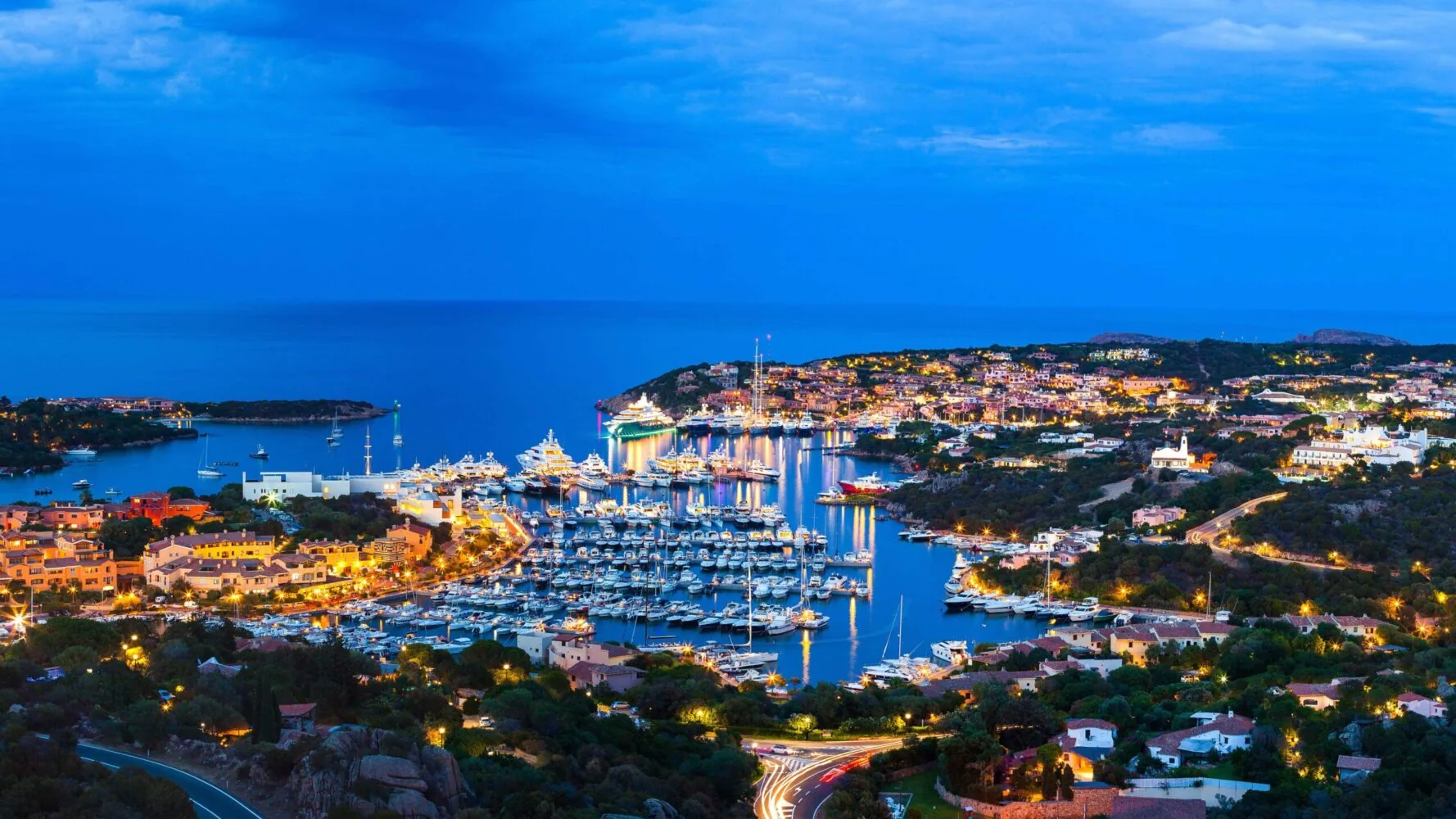Night view of Porto Cervo Marina in Sardinia, Italy, illuminated with lights and filled with luxury yachts along the Mediterranean coast.