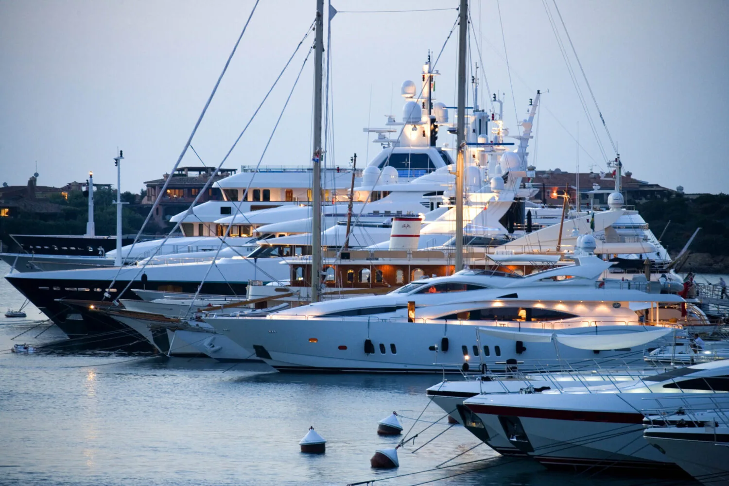 Luxury yachts moored at Porto Cervo Marina in Sardinia, Italy during twilight.