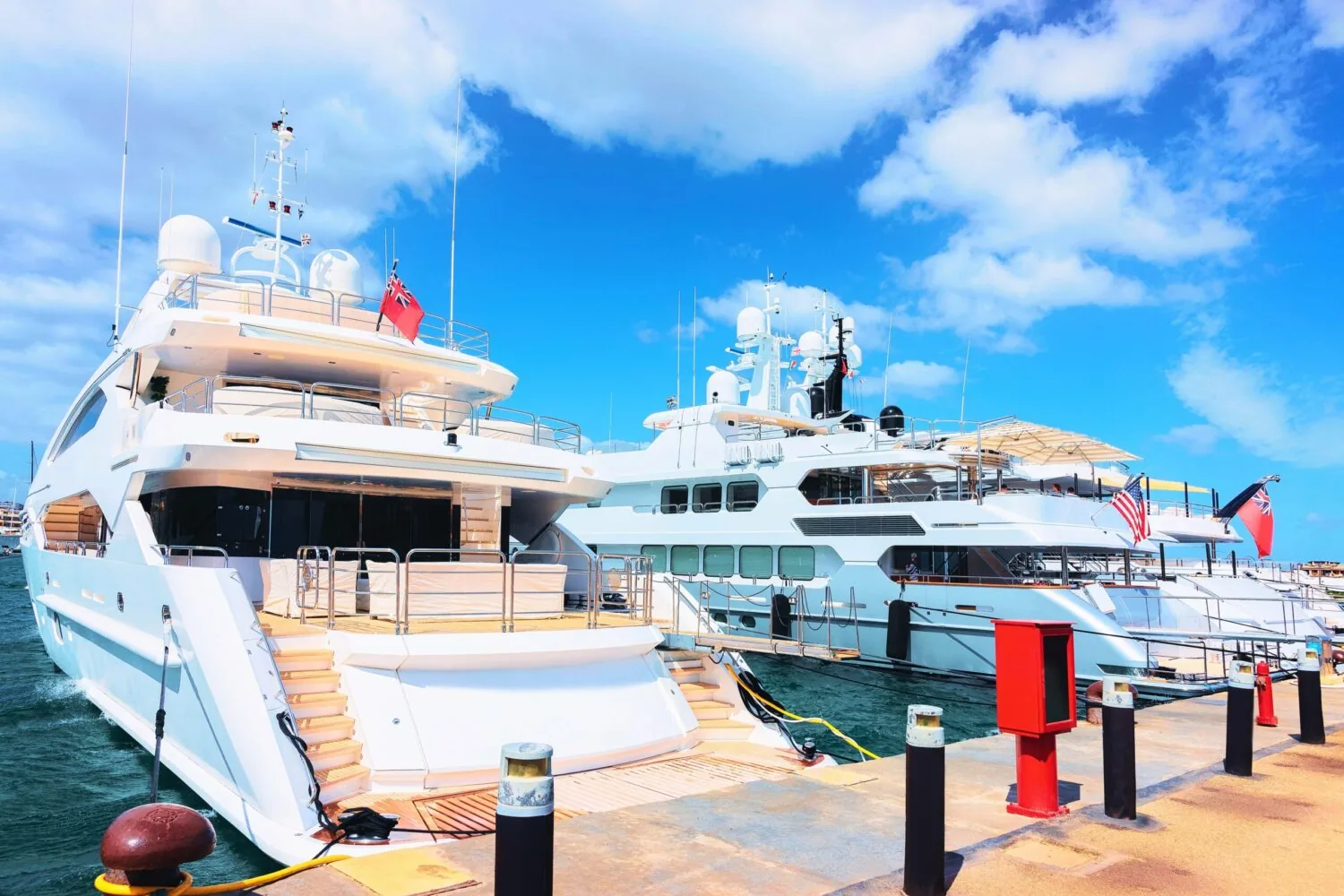Luxury megayachts docked at Porto Cervo Marina in Sardinia, Italy under a bright blue Mediterranean sky.