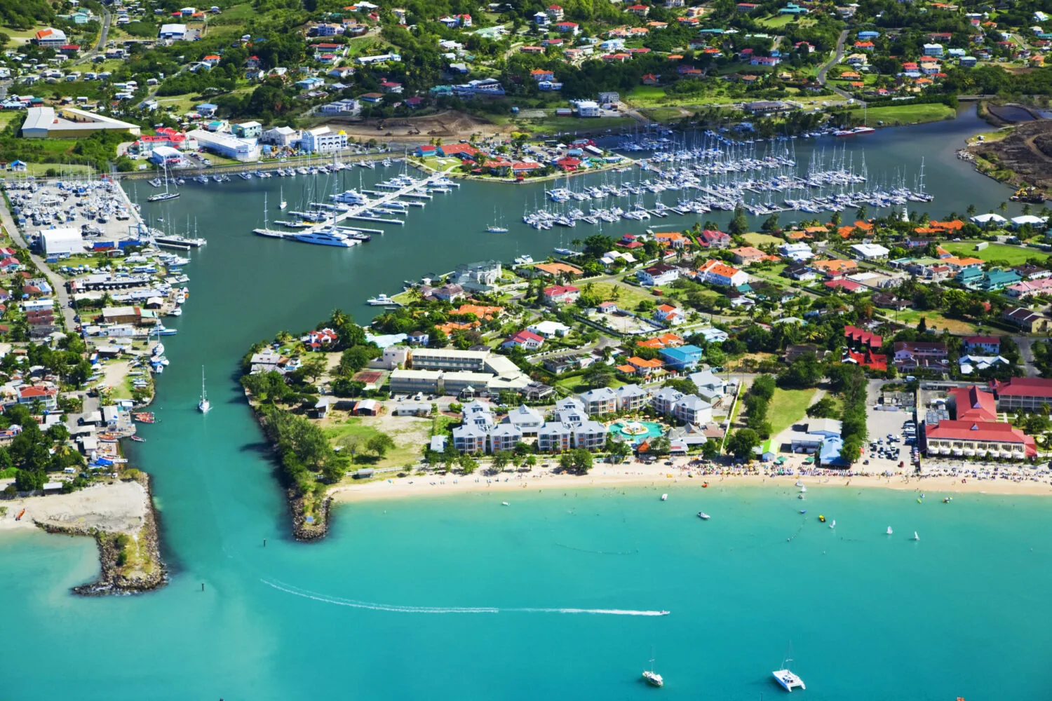 Aerial view of RBM Main marina with yachts, colorful buildings, and a vibrant beachfront.